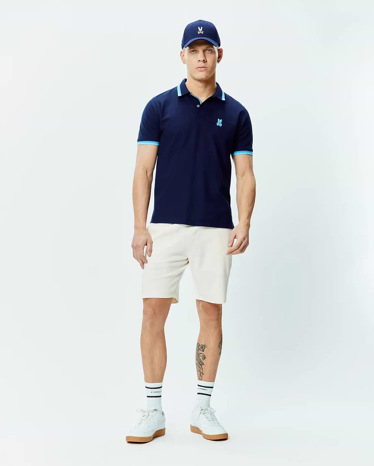 Mens Holden Pique Polo, a classic fit navy pique polo shirt with light blue trim on the collar and sleeve cuffs, featuring a small embroidered Psycho Bunny skull logo on the left chest.
