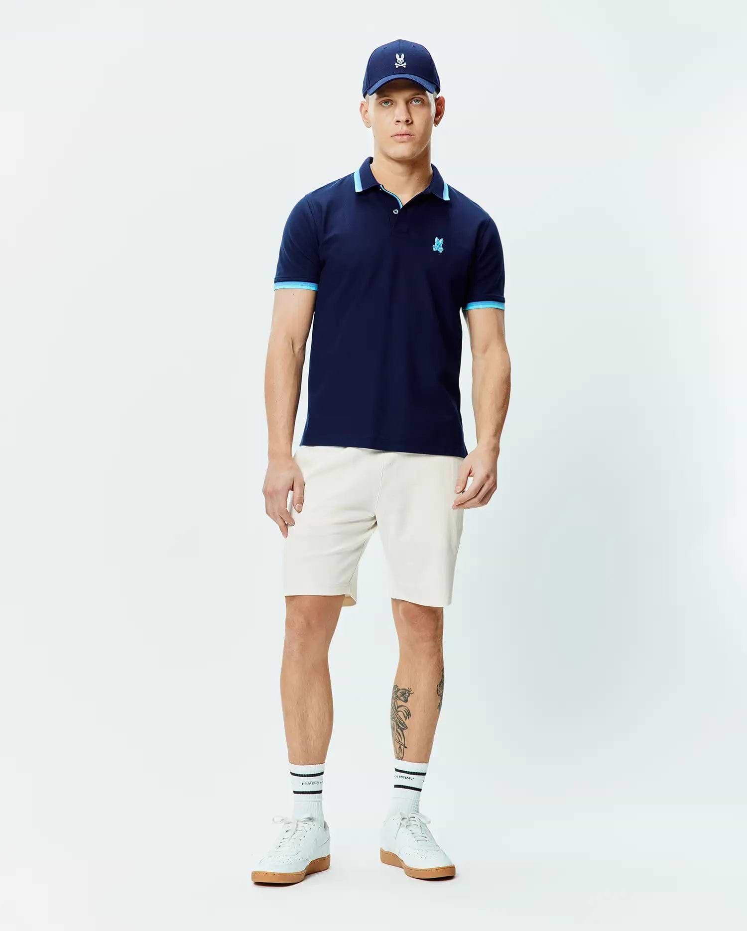 Mens Holden Pique Polo, a classic fit navy pique polo shirt with light blue trim on the collar and sleeve cuffs, featuring a small embroidered Psycho Bunny skull logo on the left chest.