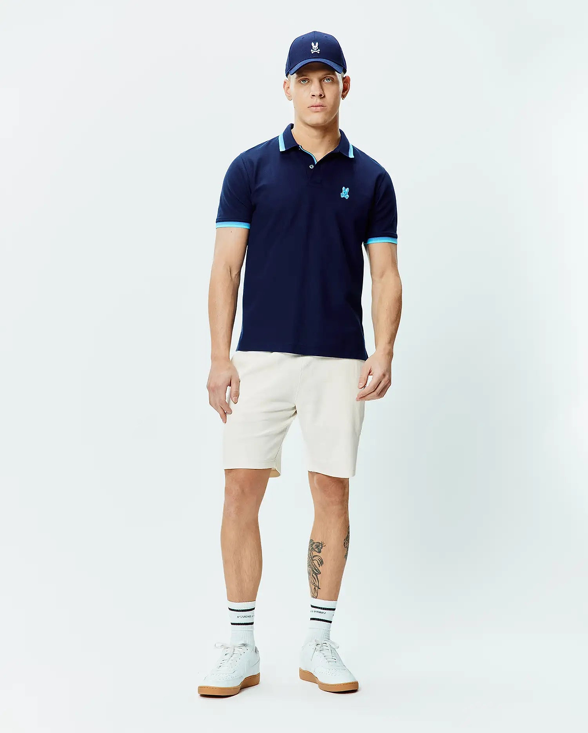 Mens Holden Pique Polo, a classic fit navy pique polo shirt with light blue trim on the collar and sleeve cuffs, featuring a small embroidered Psycho Bunny skull logo on the left chest.