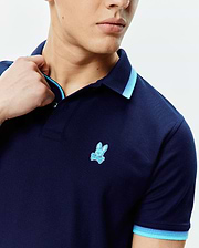 Mens Holden Pique Polo in navy pique fabric, featuring a classic fit, light blue and medium blue striped collar and sleeve cuffs, and a small embroidered Psycho Bunny skull logo on the left chest.