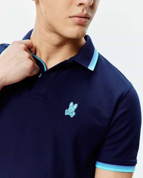 Mens Holden Pique Polo in navy pique fabric, featuring a classic fit, light blue and medium blue striped collar and sleeve cuffs, and a small embroidered Psycho Bunny skull logo on the left chest.