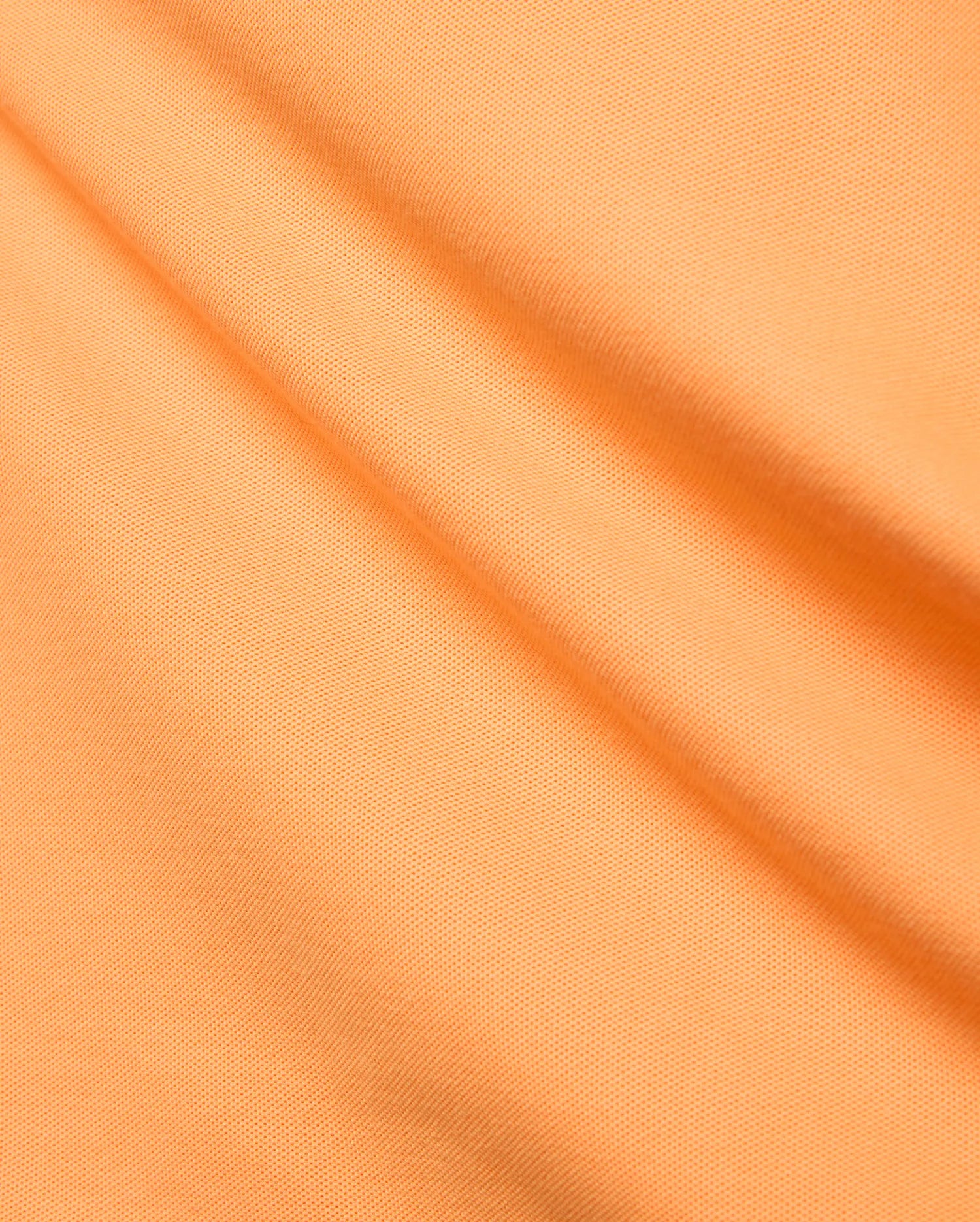 Premium Mens Holden Pique Polo by Psycho Bunny, featuring a bright peach-orange hue and finely woven, classic textured pique fabric with elegant diagonal folds.