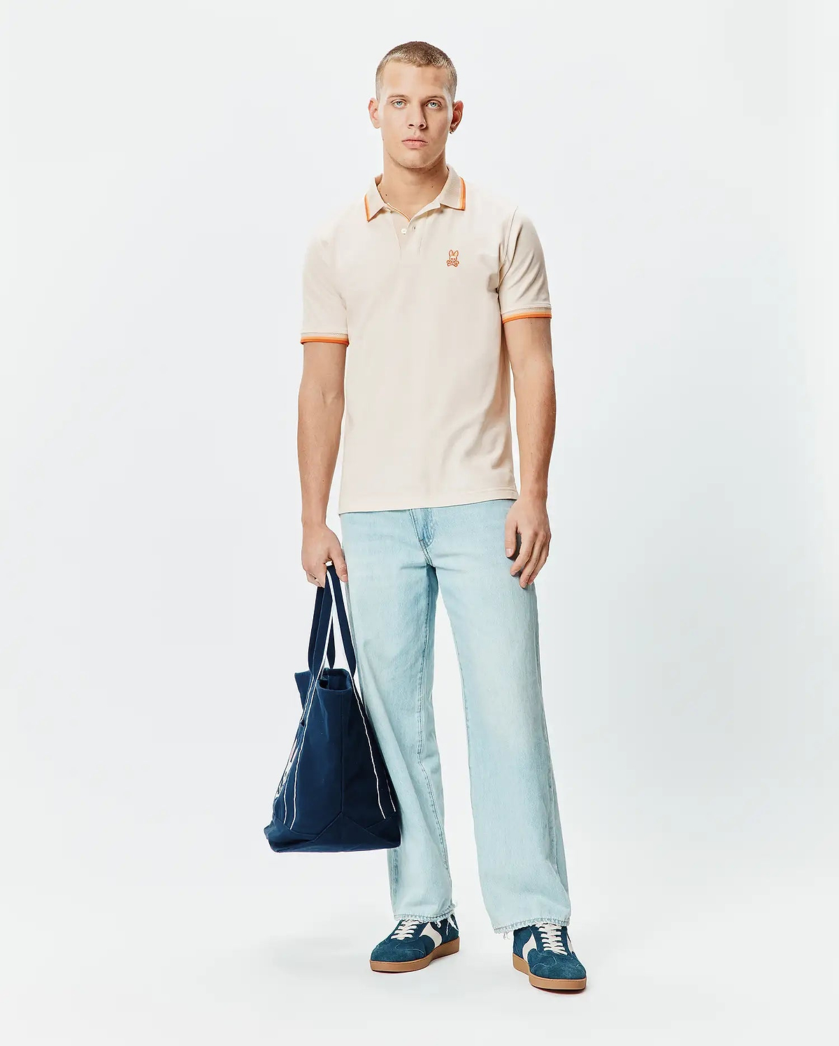 Mens Holden Pique Polo in cream, featuring a classic fit, pique texture, and orange tipping on the collar and sleeve cuffs, with a small embroidered orange Psycho Bunny skull logo on the left chest.