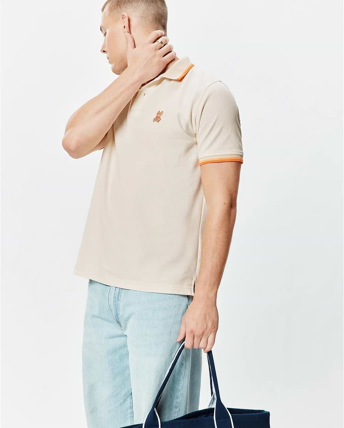 Mens Holden Pique Polo, a classic fit khaki pique knit polo with orange striped collar and sleeve cuffs, featuring a small embroidered orange Psycho Bunny skull logo on the left chest.