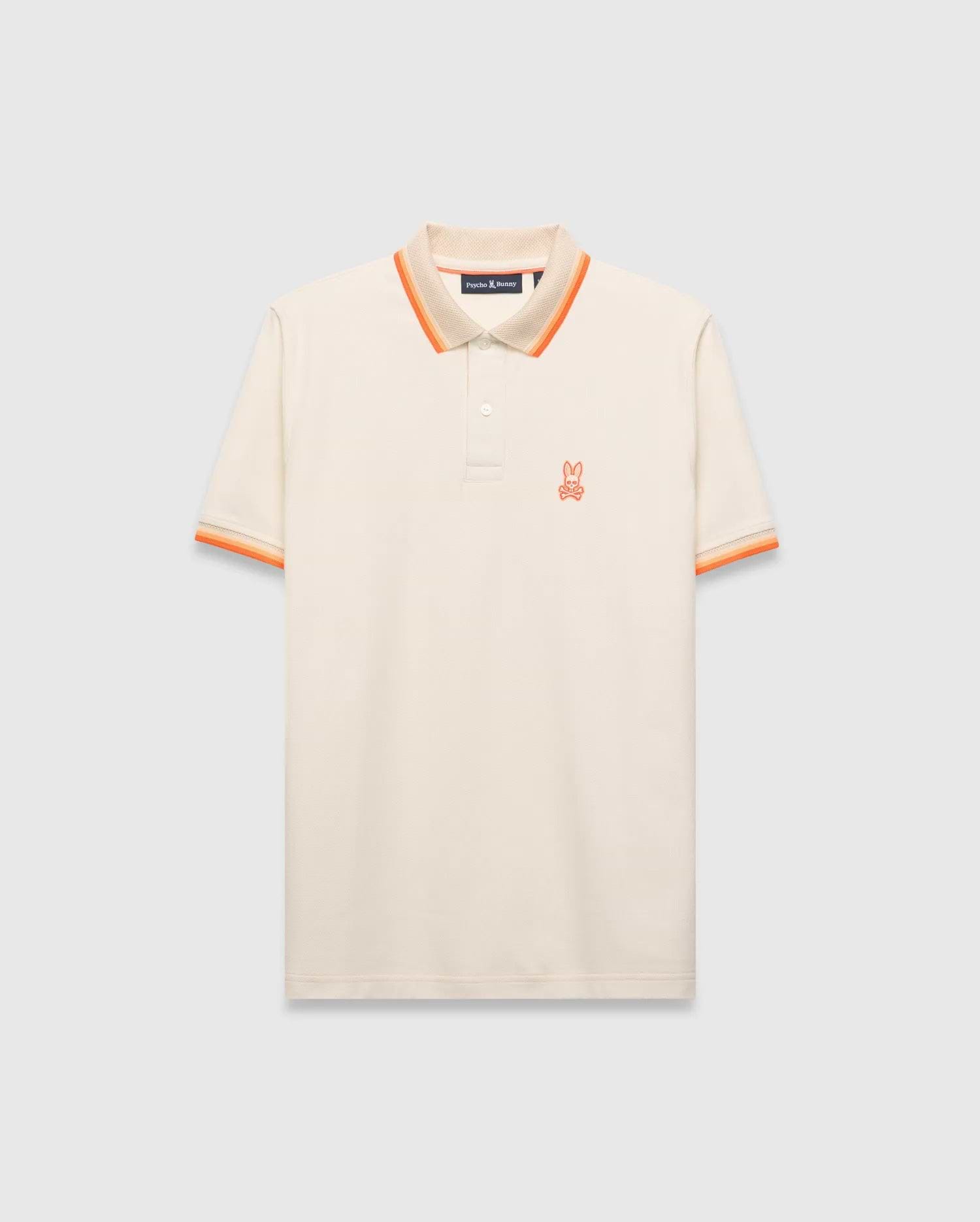 Mens Holden Pique Polo, cream classic fit with textured pique fabric, featuring an orange embroidered Psycho Bunny skull logo on the left chest, and ribbed collar/cuffs with orange and beige stripes.