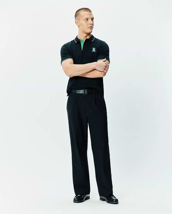 Mens Nate Pique Polo, a classic fit black pique polo shirt with a vibrant green collar, white tipping on the collar and sleeves, and an embroidered Psycho Bunny skull logo on the left chest.