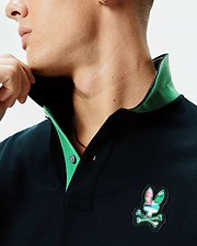 Mens Nate Pique Polo, a dark navy classic fit pique polo featuring a vibrant green contrast collar and a prominent multi-color embroidered Psycho Bunny skull logo on the chest.