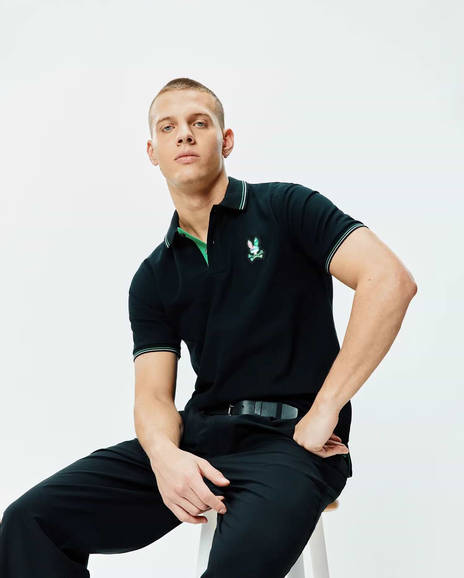 Black Mens Nate Pique Polo, classic fit pique knit, featuring a vibrant embroidered Psycho Bunny logo on the left chest, with green undercollar and white/green tipped ribbed collar and cuffs.