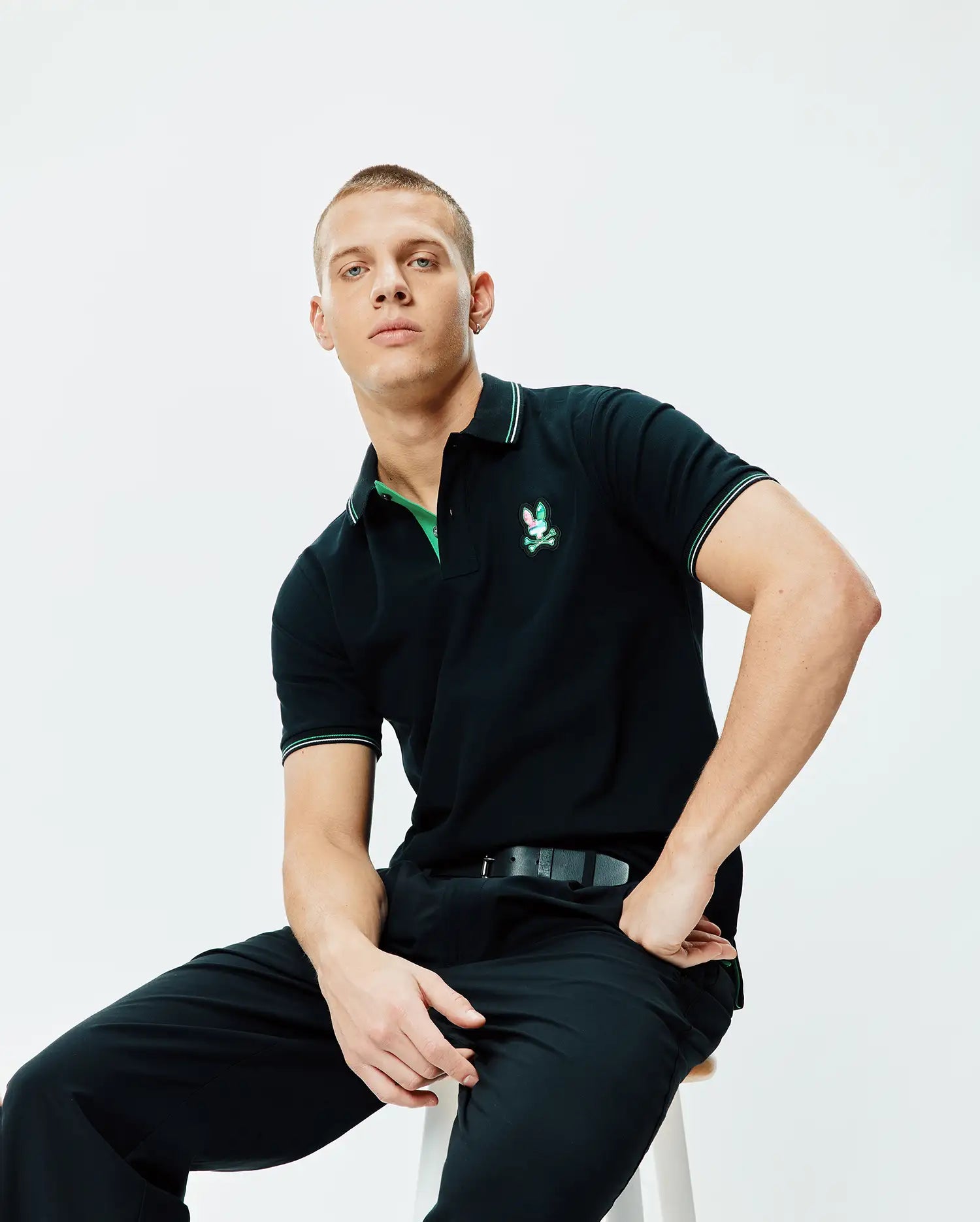 Black Mens Nate Pique Polo, classic fit pique knit, featuring a vibrant embroidered Psycho Bunny logo on the left chest, with green undercollar and white/green tipped ribbed collar and cuffs.