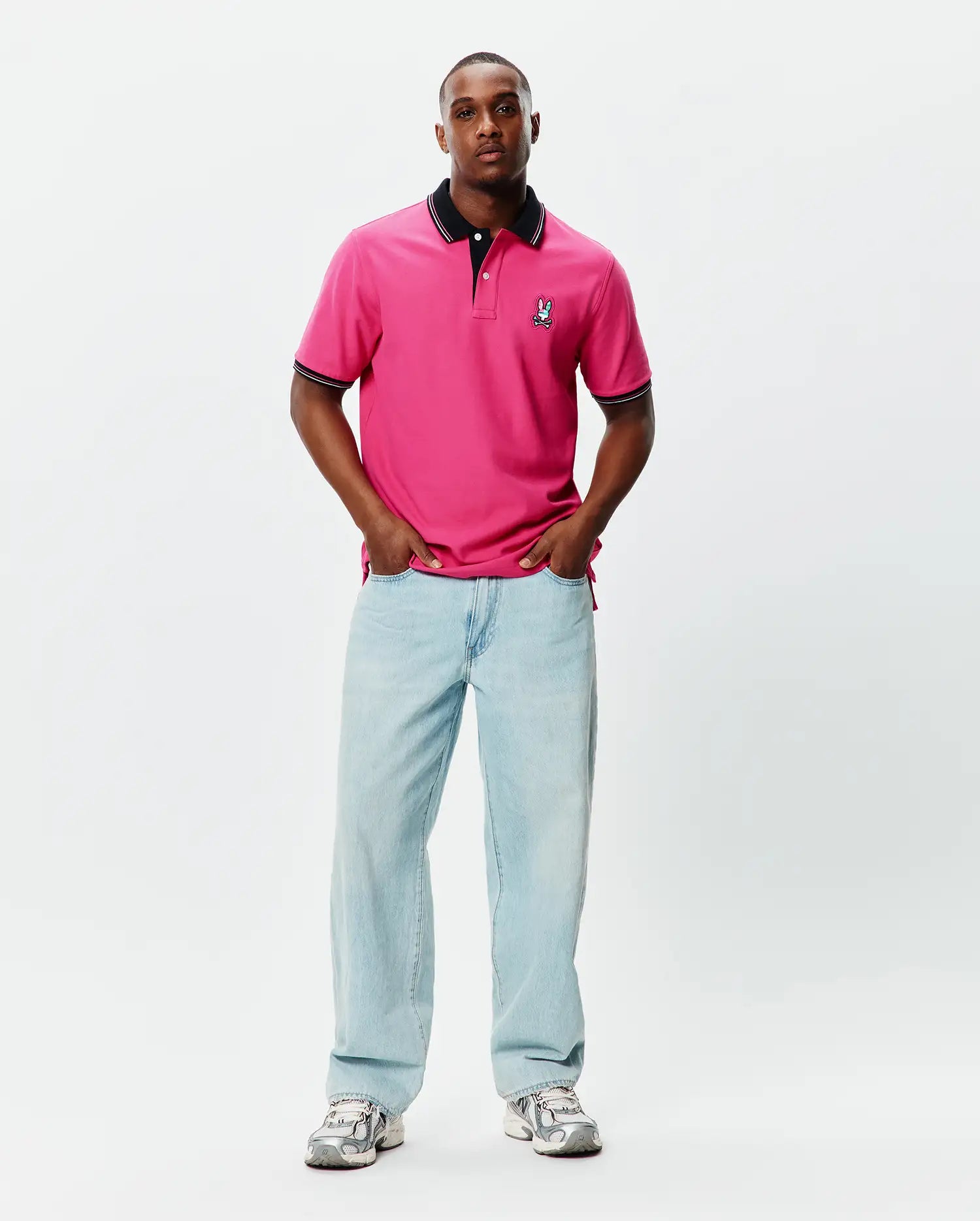 Mens Nate Pique Polo in vibrant pink, featuring a classic fit, black ribbed collar and cuffs with white tipping, and a small embroidered Psycho Bunny skull logo on the left chest.