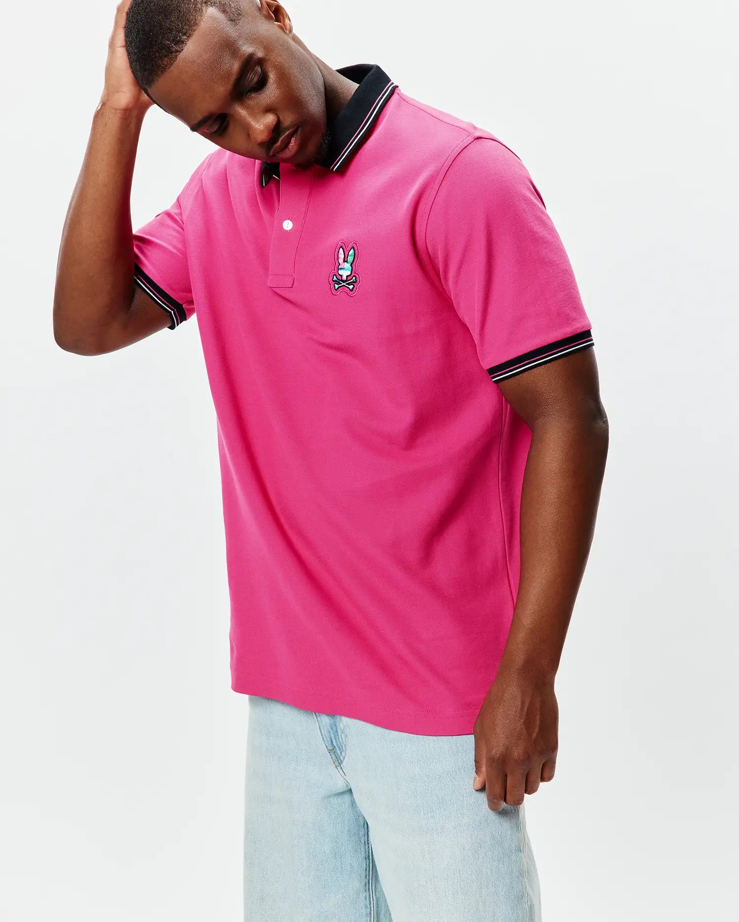 Mens Nate Pique Polo in hot pink, classic fit, pique fabric, with black ribbed collar and cuffs featuring white tipping, and a small embroidered multi-color Psycho Bunny skull logo on the left chest.