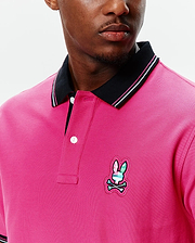 MENS NATE PIQUE POLO in hot pink pique, with a black ribbed collar featuring white and pink stripes, a two-button placket, and a multi-color embroidered Psycho Bunny skull logo on the left chest.