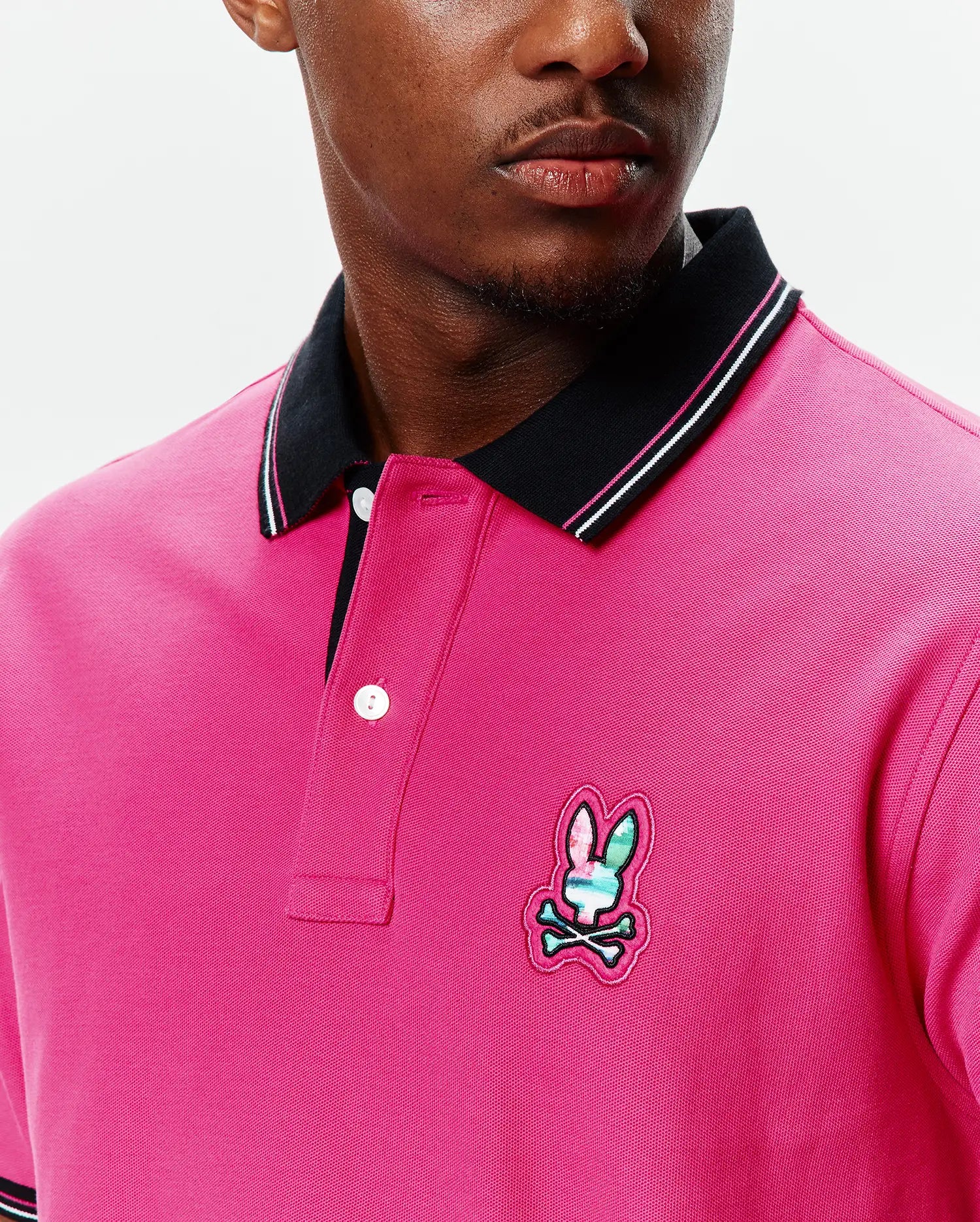 MENS NATE PIQUE POLO in hot pink pique, with a black ribbed collar featuring white and pink stripes, a two-button placket, and a multi-color embroidered Psycho Bunny skull logo on the left chest.