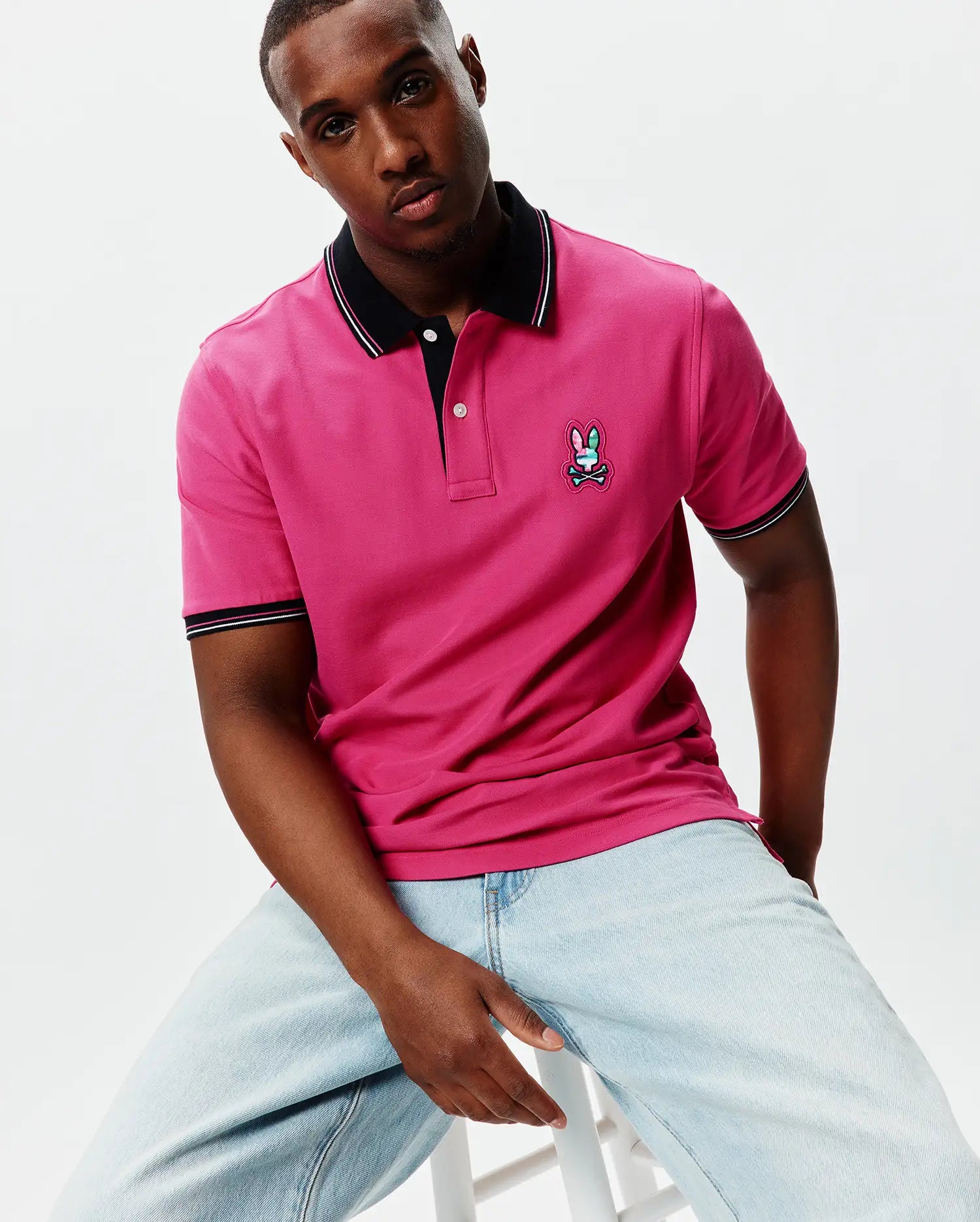 Mens Nate Pique Polo in vibrant fuchsia, featuring a classic fit, black ribbed collar and cuffs with white and pink tipping, and a colorful embroidered Psycho Bunny skull logo on the left chest.