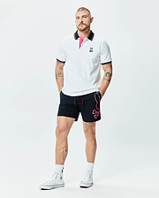 White Mens Nate Pique Polo with black collar, pink under-collar, striped cuffs, and embroidered Psycho Bunny logo, paired with black shorts featuring a large pink Psycho Bunny skull graphic.