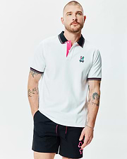 Mens Nate Pique Polo, a white classic fit pique polo with black collar and cuffs featuring pink and white tipping, hot pink placket lining, and a small embroidered multi-color Psycho Bunny skull logo on the left chest.