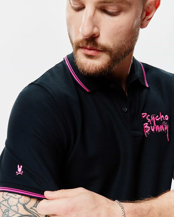 Mens Duncan Pique Polo, black classic fit pique polo with hot pink tipping on collar and cuffs, featuring a small embroidered pink bunny skull on the left sleeve and a large distressed pink Psycho Bunny text logo on the right chest.