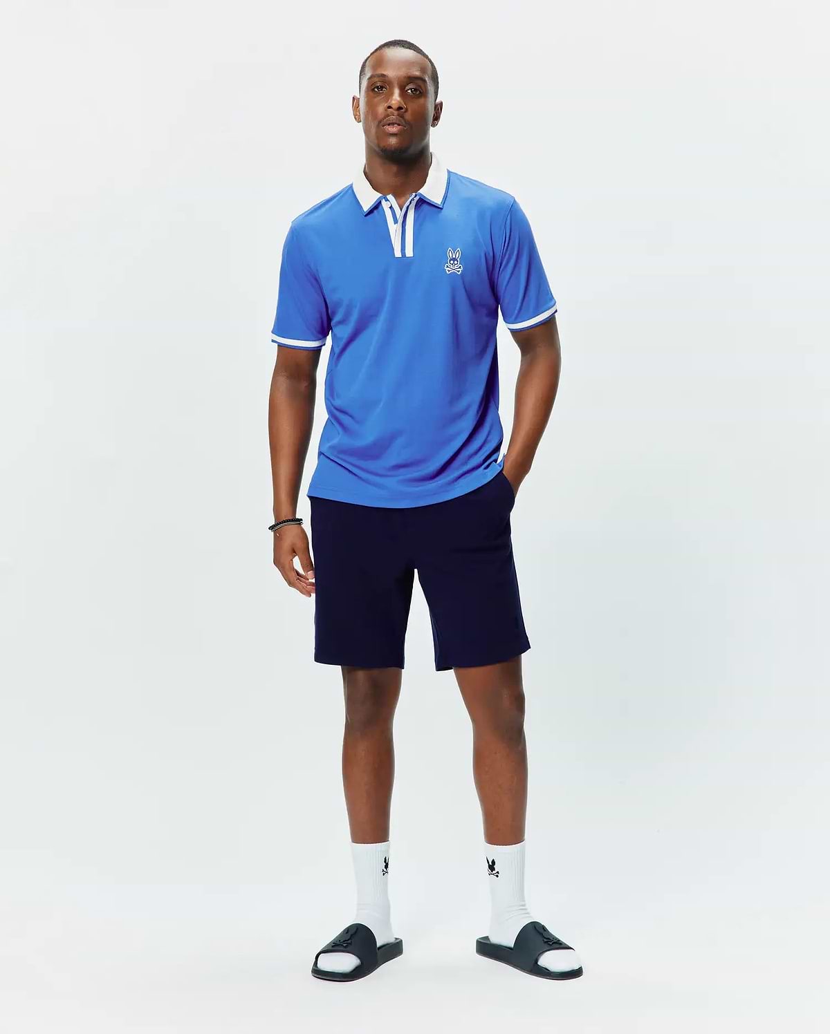 Mens Ridley Pique Polo, a bright blue classic fit pique polo shirt featuring a crisp white collar, white sleeve cuffs with tipping, and a small embroidered white Psycho Bunny skull logo on the left chest.
