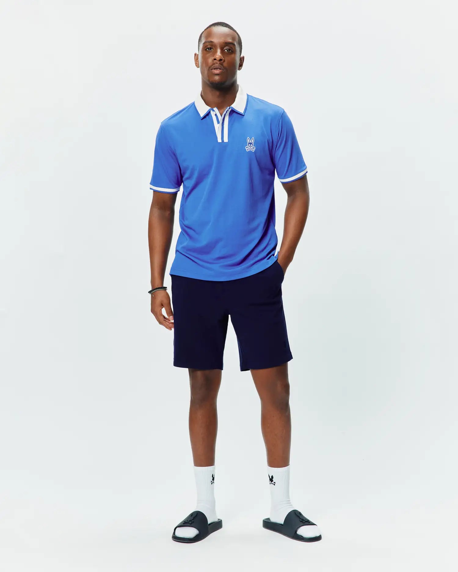 Mens Ridley Pique Polo, a bright blue classic fit pique polo shirt featuring a crisp white collar, white sleeve cuffs with tipping, and a small embroidered white Psycho Bunny skull logo on the left chest.