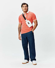 Mens Ridley Pique Polo in coral, featuring a classic fit, pique fabric, white contrast collar, white double-stripe ribbed cuffs, and a small embroidered Psycho Bunny skull logo on the left chest.