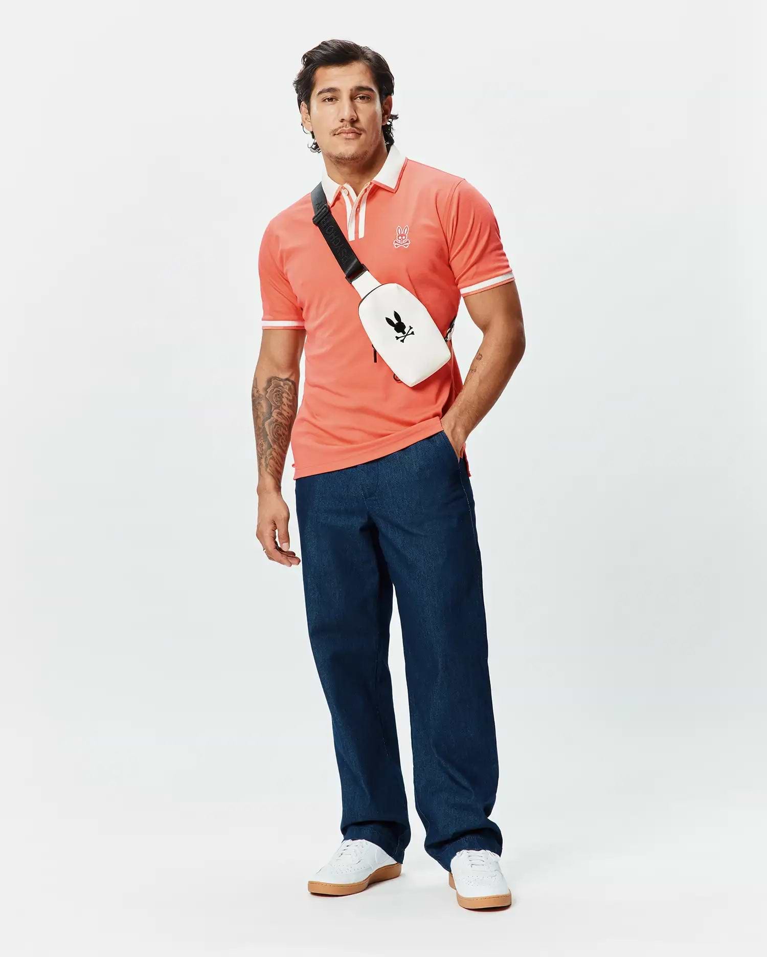 Mens Ridley Pique Polo in coral, featuring a classic fit, pique fabric, white contrast collar, white double-stripe ribbed cuffs, and a small embroidered Psycho Bunny skull logo on the left chest.