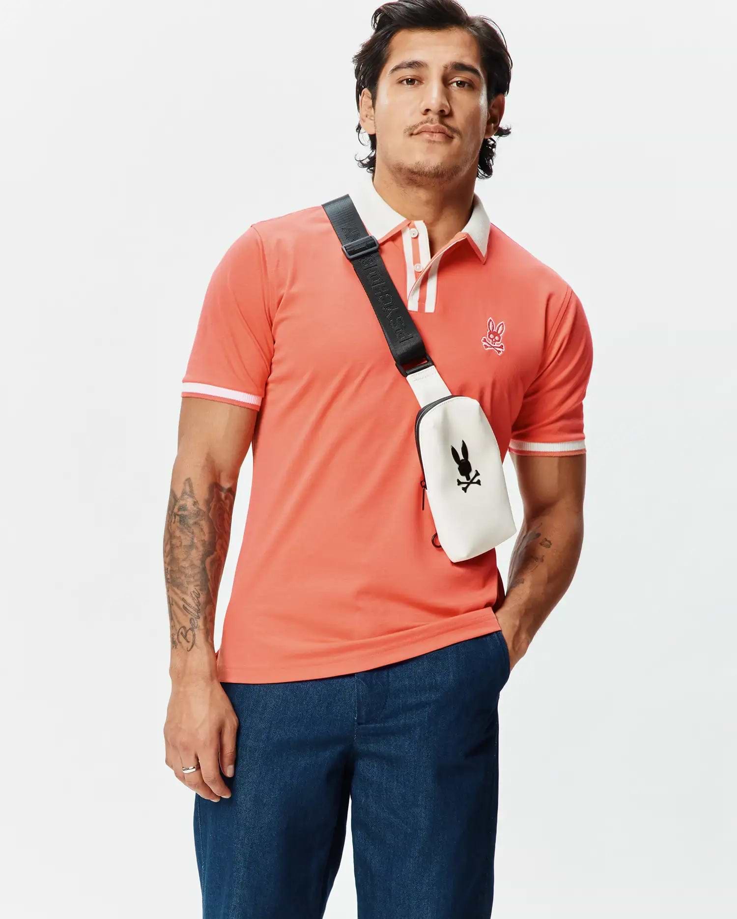 Mens Ridley Pique Polo in vibrant coral, classic fit pique fabric with white ribbed collar and cuffs, featuring a small embroidered Psycho Bunny skull logo on the left chest.