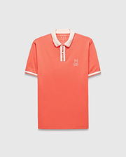 Mens Ridley Pique Polo in coral pique, featuring a classic fit, cream ribbed collar and cuffs with stripes, a two-button placket with cream stripe, and an embroidered white Psycho Bunny skull logo on the left chest.