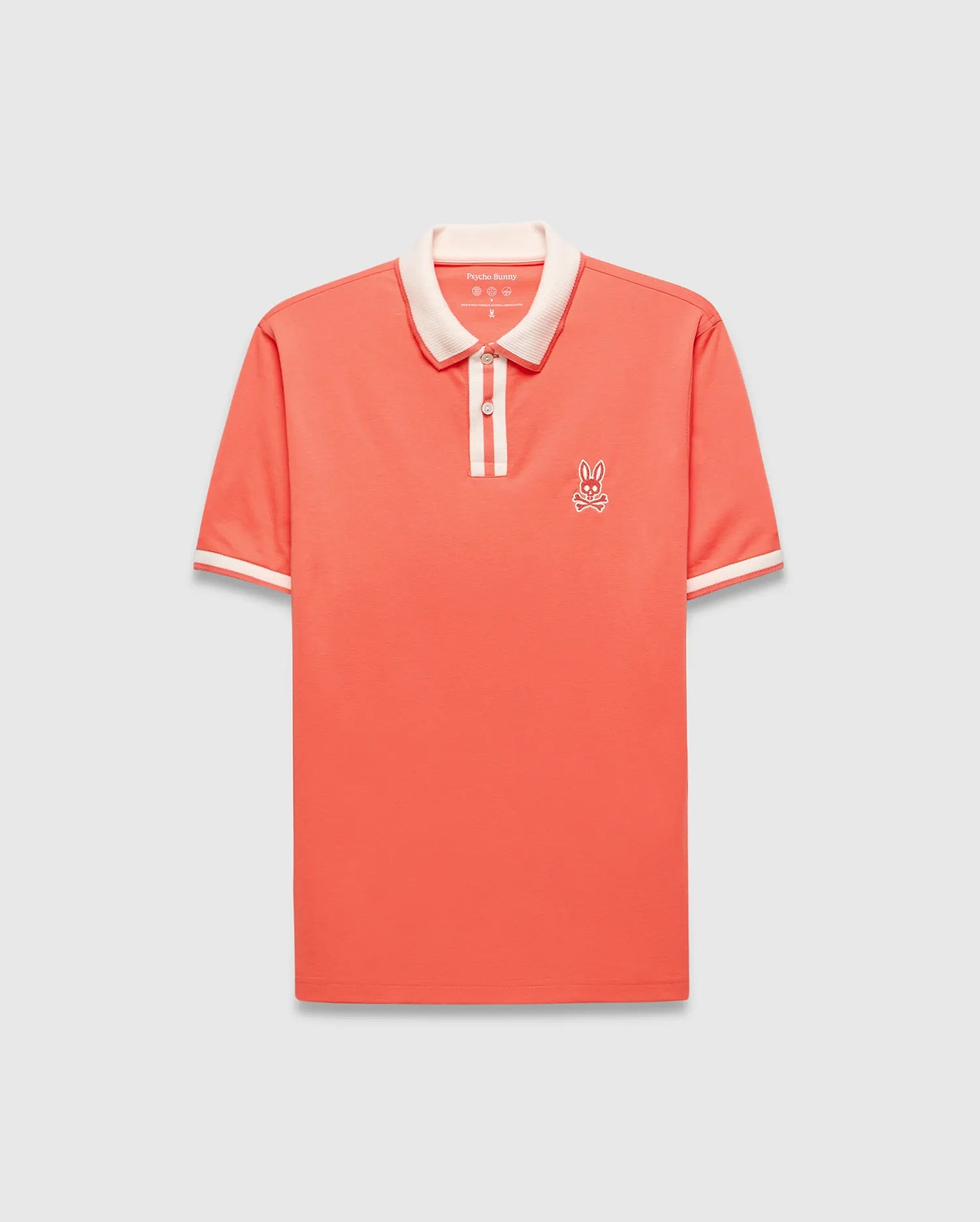 Mens Ridley Pique Polo in coral pique, featuring a classic fit, cream ribbed collar and cuffs with stripes, a two-button placket with cream stripe, and an embroidered white Psycho Bunny skull logo on the left chest.