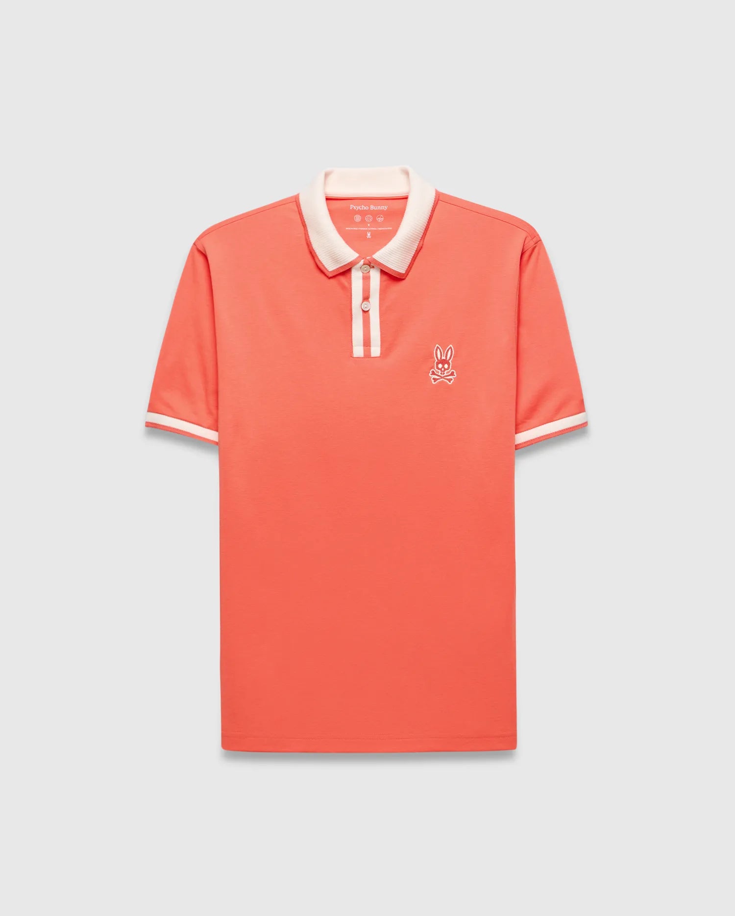 Mens Ridley Pique Polo in coral pique, featuring a classic fit, cream ribbed collar and cuffs with stripes, a two-button placket with cream stripe, and an embroidered white Psycho Bunny skull logo on the left chest.