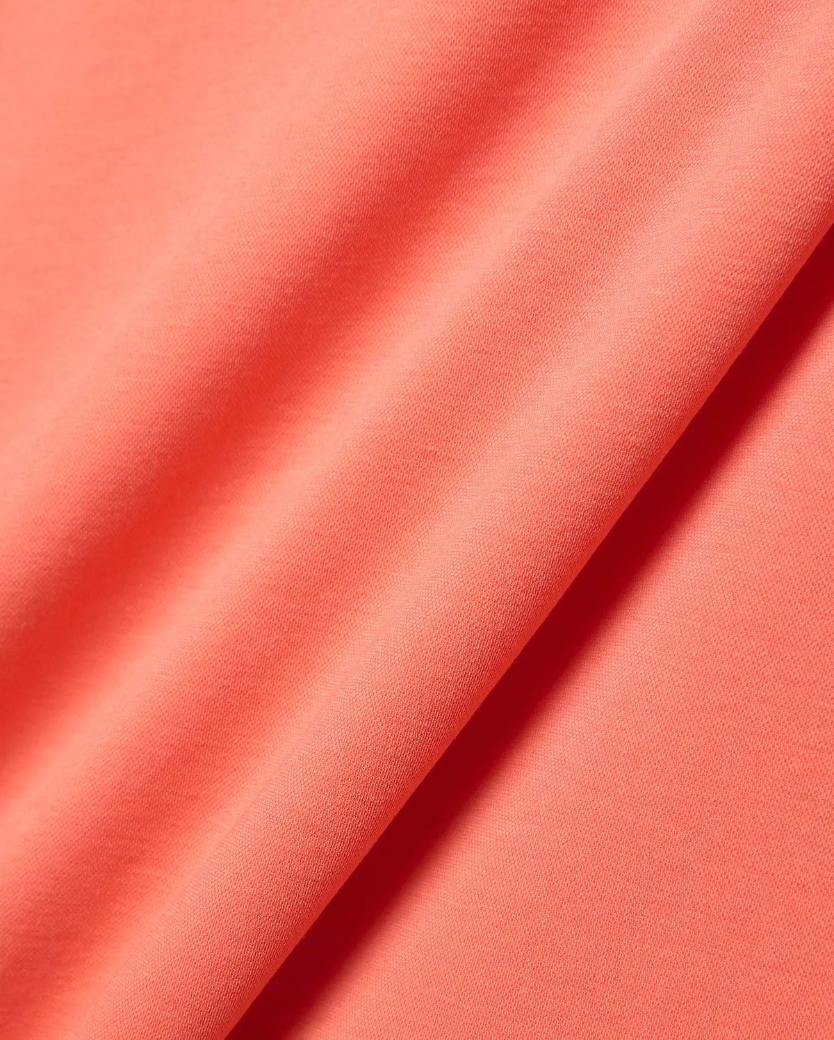 Close-up of the vibrant coral Mens Ridley Pique Polo fabric, featuring a distinct, premium textured pique knit, embodying Psycho Bunny's refined streetwear aesthetic.