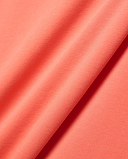 Close-up of the vibrant coral Mens Ridley Pique Polo fabric, featuring a distinct, premium textured pique knit, embodying Psycho Bunny's refined streetwear aesthetic.