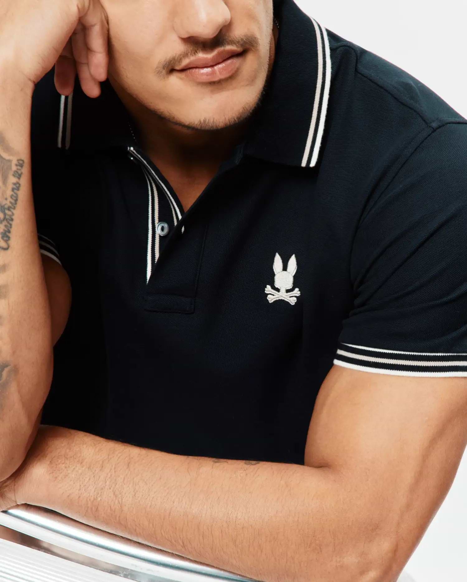 Mens Brad Pique Polo, a classic fit navy pique polo shirt with white double-striped collar and sleeve cuffs, featuring a small embroidered white Psycho Bunny skull logo on the left chest.