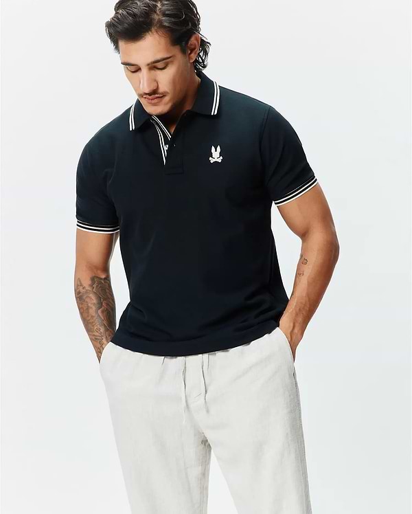 Mens Brad Pique Polo, a classic fit navy pique polo shirt with white striped collar and cuffs, featuring a small embroidered white Psycho Bunny skull logo on the left chest.