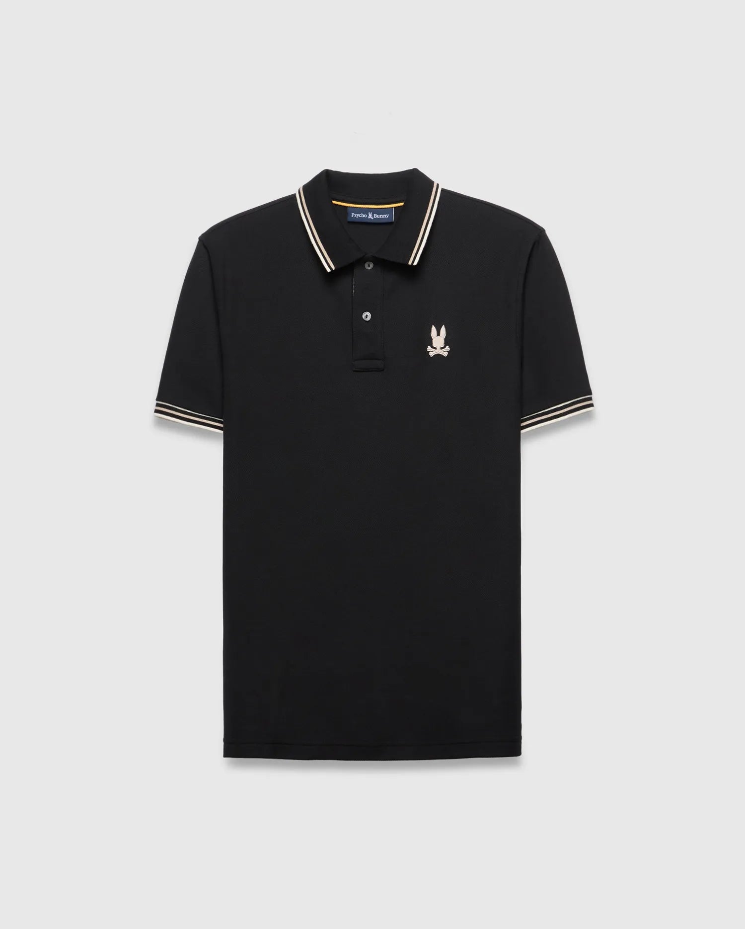 Mens Brad Pique Polo, black classic fit with white and gold striped collar and cuffs, featuring a small embroidered light pink/cream Psycho Bunny skull logo on the left chest.