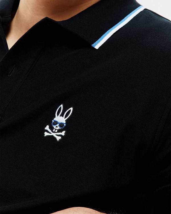Mens Sunny Pique Polo, black classic fit pique polo with a ribbed collar featuring white and blue stripes, and a small embroidered Psycho Bunny skull logo with blue sunglasses on the left chest.