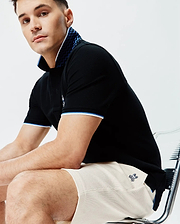 Mens Sunny Pique Polo in black, featuring a classic fit, white collar with a bold blue zigzag pattern, blue and white striped cuffs, and a small embroidered Psycho Bunny skull logo on the left chest.