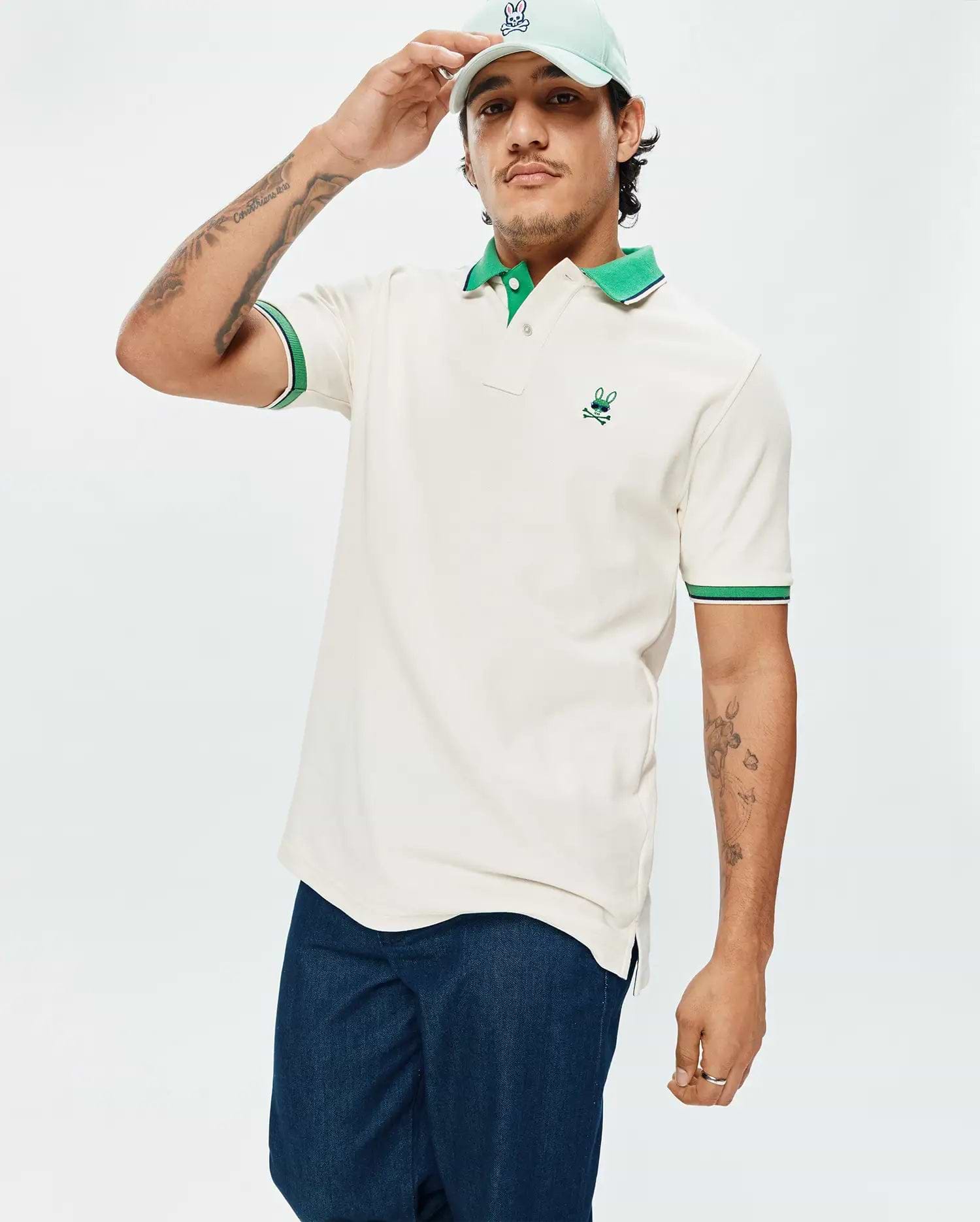 Mens Sunny Pique Polo in cream pique, featuring a classic fit, vibrant green collar, green and navy striped sleeve cuffs, and a small embroidered green Psycho Bunny skull logo on the left chest.