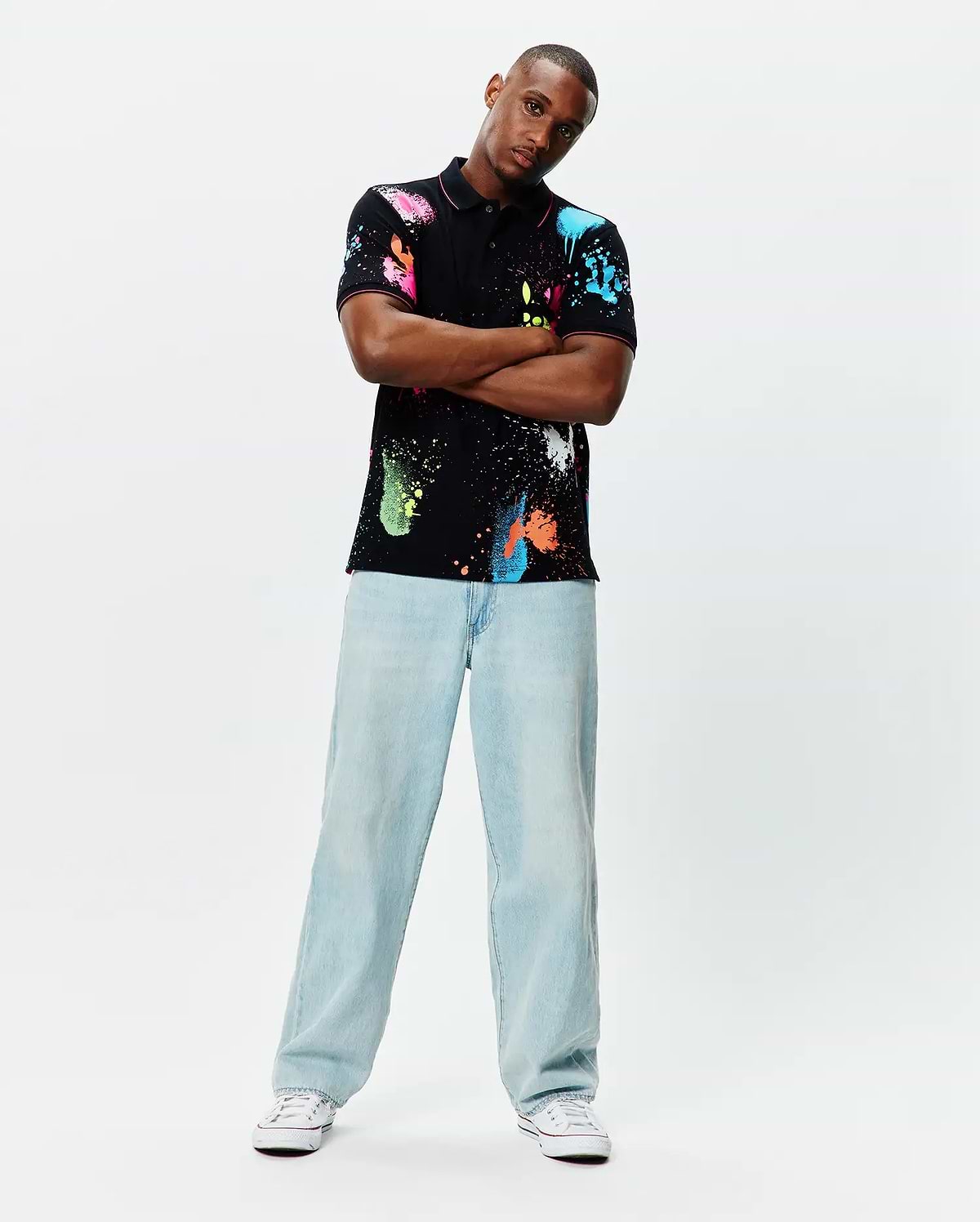 Quintin Aop Pique Polo: Black classic fit pique polo with vibrant all-over neon paint splatter print in pink, blue, green, orange, and white, featuring a small embroidered Psycho Bunny skull logo on the left chest.