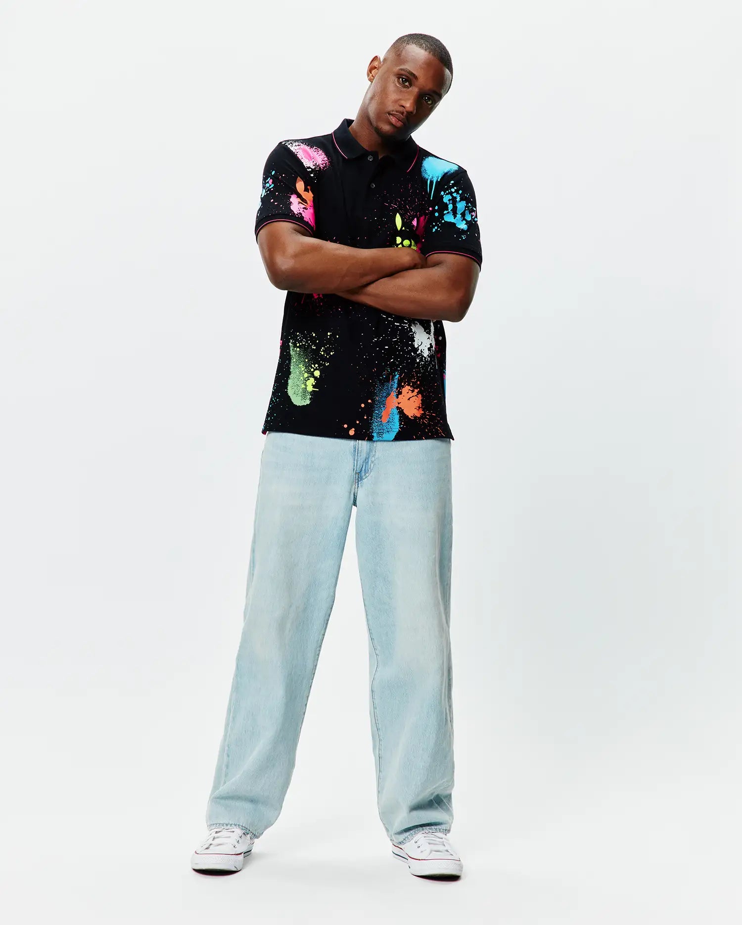 Quintin Aop Pique Polo: Black classic fit pique polo with vibrant all-over neon paint splatter print in pink, blue, green, orange, and white, featuring a small embroidered Psycho Bunny skull logo on the left chest.