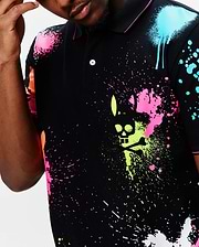 Mens Quintin Aop Pique Polo, a black pique polo with a vibrant all-over neon paint splatter print in pink, lime, blue, and orange, featuring a large central Psycho Bunny skull logo graphic.
