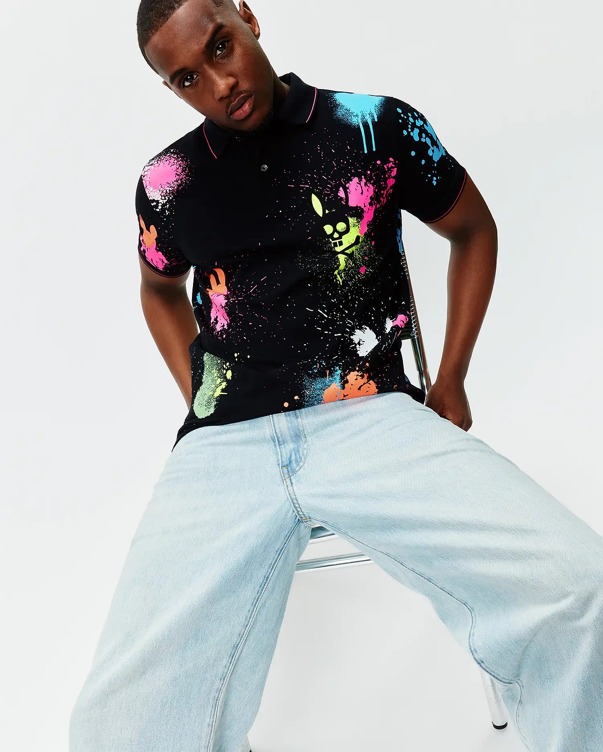 Mens Quintin Aop Pique Polo, a black classic fit pique polo with vibrant neon pink, blue, green, orange, and white paint splatter print, featuring the Psycho Bunny skull logo integrated into the design and pink trim.