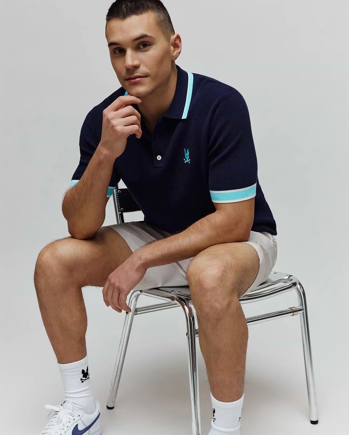 MENS DAX KNIT POLO in navy, a classic fit knit polo with light blue and white striped collar and cuffs, featuring a small embroidered Psycho Bunny skull logo on the left chest. (1)
