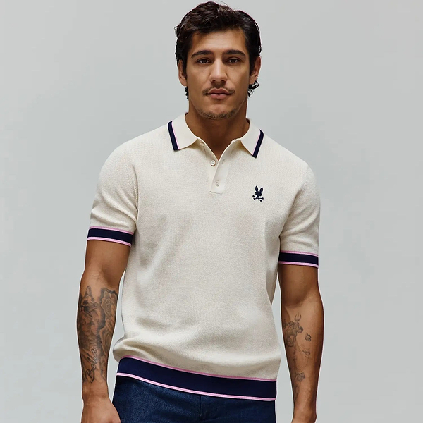 Mens Dax Knit Polo, cream pique knit with classic fit, featuring navy and pink tipped collar, cuffs, and hem, plus a small embroidered navy Psycho Bunny skull logo on the left chest.