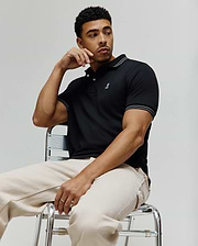 Black Mens Kenyon Lightweight Pique Polo, classic fit, with white striped ribbed collar and cuffs, and a small embroidered pink and white Psycho Bunny skull logo on the left chest.