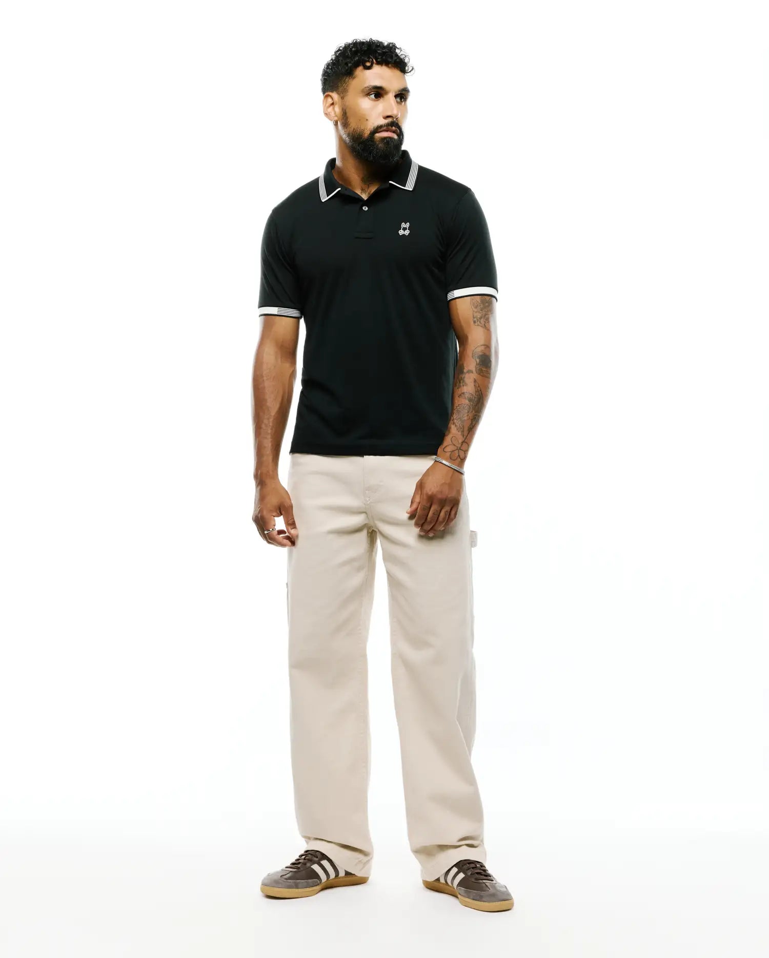 Black Mens Timmy Interlock Polo, classic fit, smooth interlock fabric, white tipped collar and striped cuffs, with a small embroidered Psycho Bunny skull logo on the left chest.