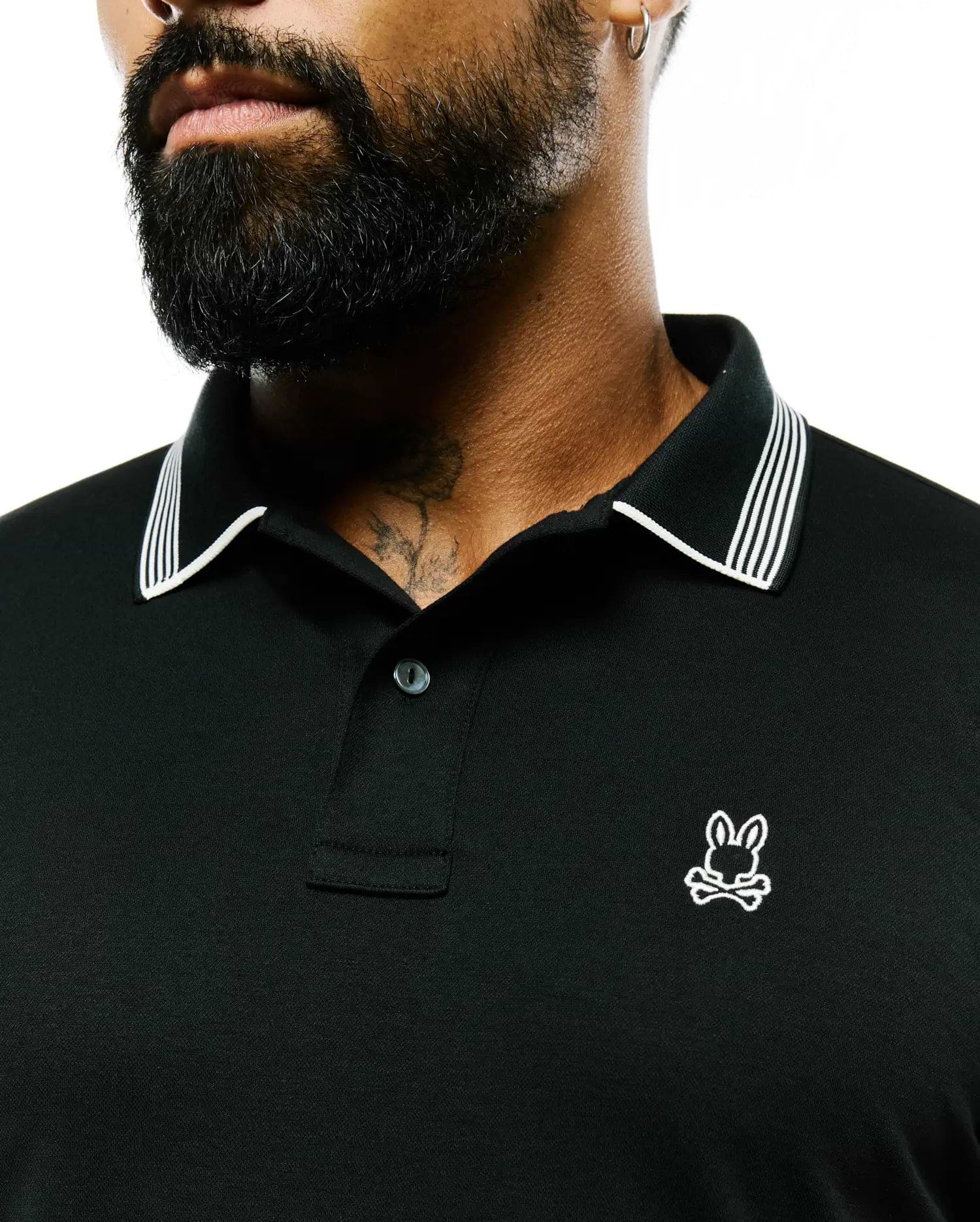 Mens Timmy Interlock Polo, a black interlock polo shirt with a classic fit, featuring a white striped collar, two-button placket, and a small embroidered white Psycho Bunny skull logo on the left chest.
