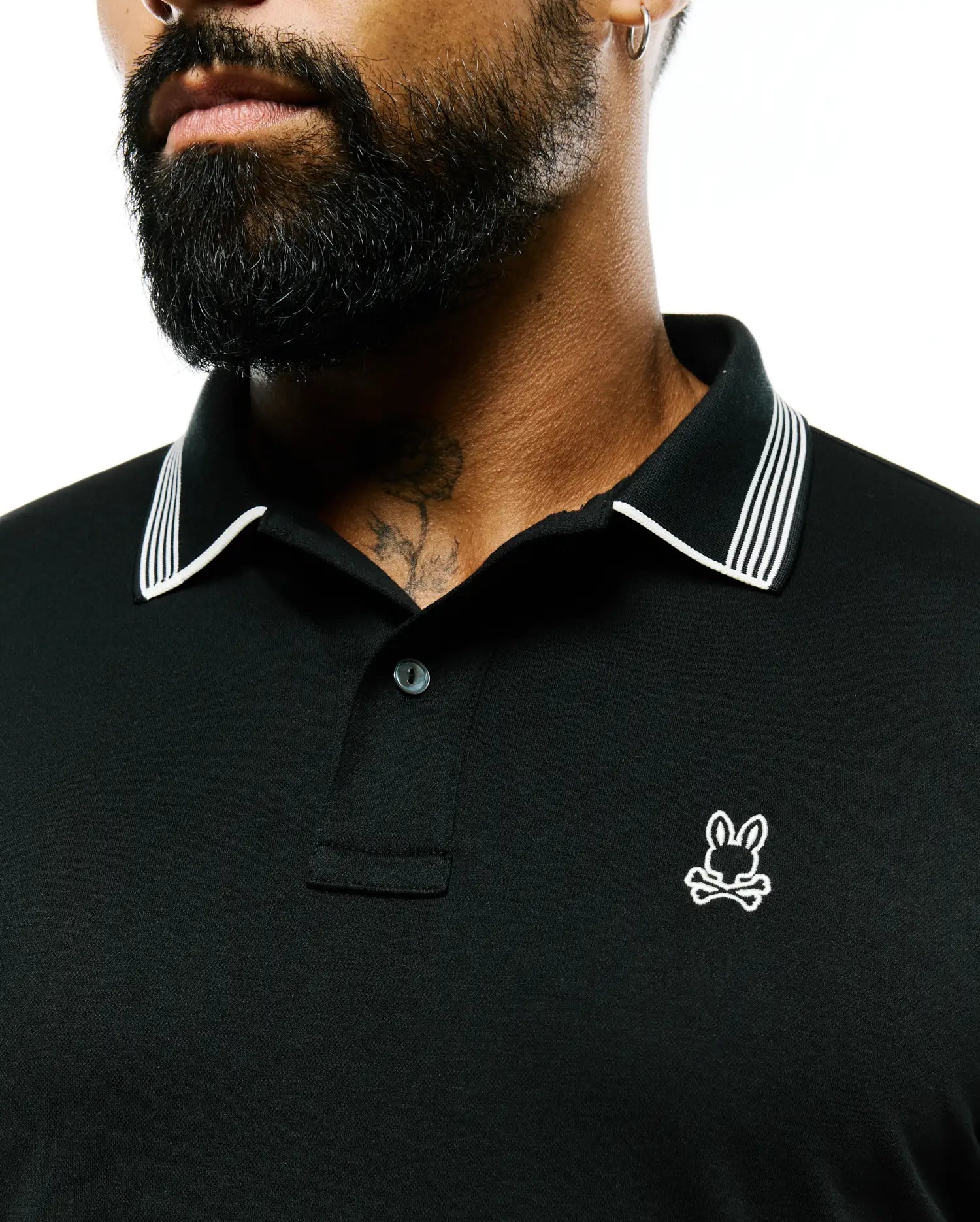 Mens Timmy Interlock Polo, a black interlock polo shirt with a classic fit, featuring a white striped collar, two-button placket, and a small embroidered white Psycho Bunny skull logo on the left chest.