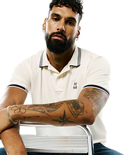 Mens Timmy Interlock Polo in cream, featuring a classic fit, smooth interlock knit, navy blue striped collar and cuffs, and a small embroidered Psycho Bunny skull logo on the left chest.