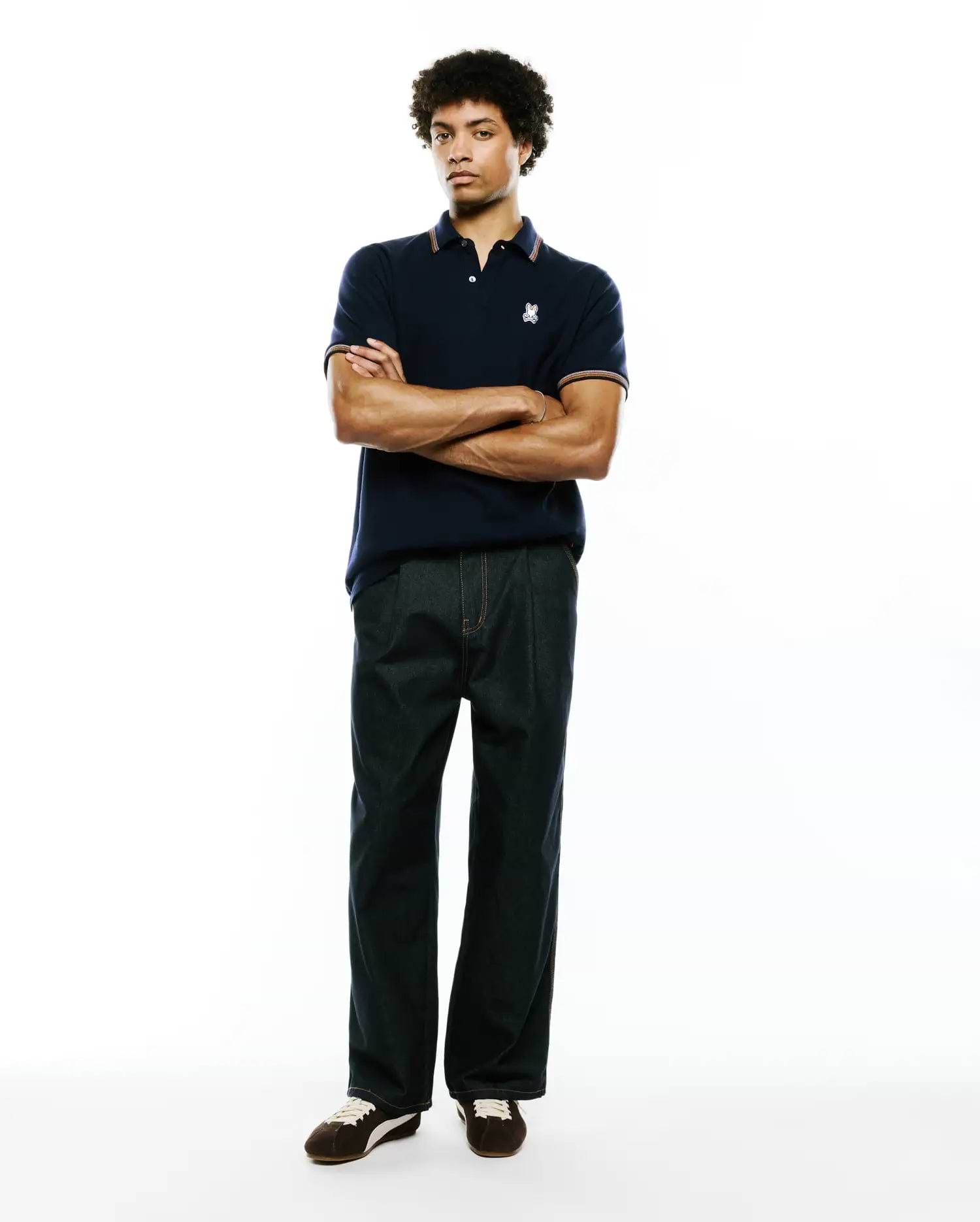 Mens Jaydon Pique Polo in navy blue, featuring a classic fit, textured pique fabric, and a small embroidered white Psycho Bunny skull logo on the left chest, accented with orange and white striped collar and cuffs.