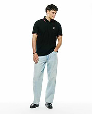 Mens Jaydon Pique Polo, a classic fit black pique polo with a small embroidered white and red Psycho Bunny skull logo on the left chest, featuring red and white striped collar and sleeve cuffs.